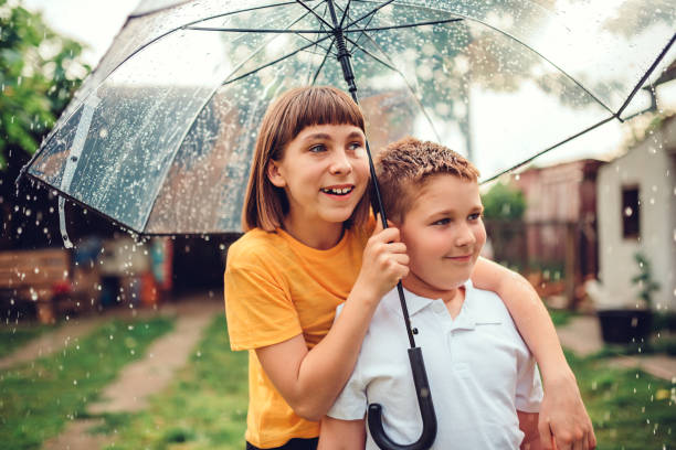 Brother and sister standing underneath umbrella