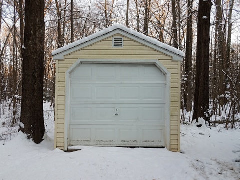 yellow garage with white door and snow and trees in the forest