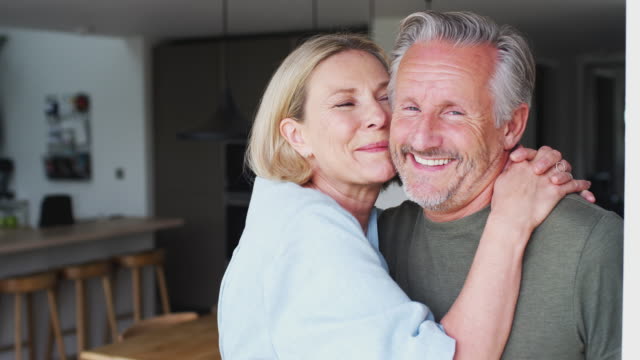 Portrait Of Loving Senior Couple Standing In Kitchen Together