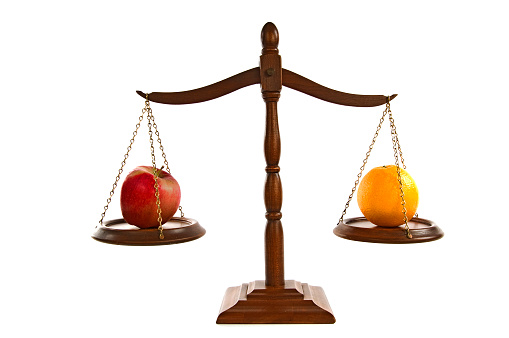 Horizontal shot of wooden scales of justice in balance.  There is an apple on one side and an orange on the other.  White background.