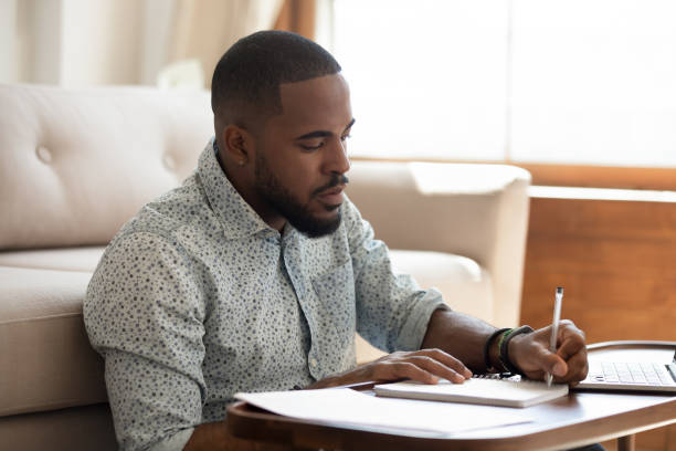 istock Serious african student writing notes studying at home with laptop 1170519314