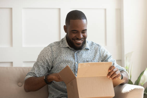 boîte en carton ouverte ouverte de consommateur d'homme africain de sourire obtiennent le colis postal - box open merchandise gift photos et images de collection