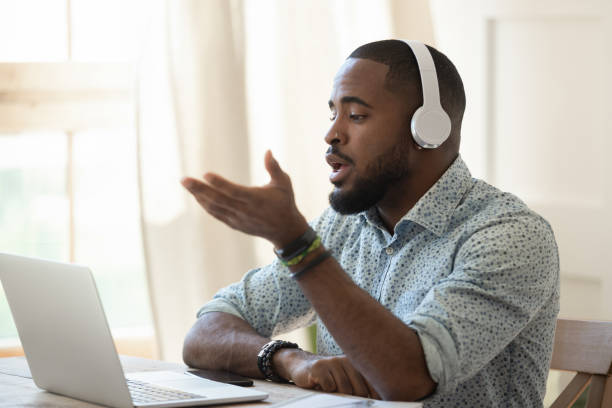 auscultadores desgastando do professor do skype do macho africano que falam olhando o portátil - skype - fotografias e filmes do acervo