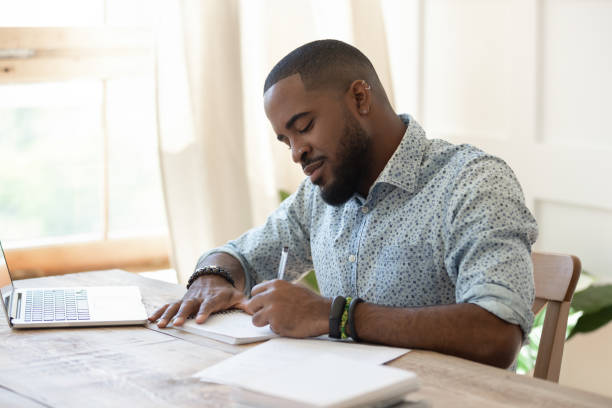 skoncentrowany african man student freelancer robi notatki studiuje z laptopem - letter writing note pad handwriting zdjęcia i obrazy z banku zdjęć