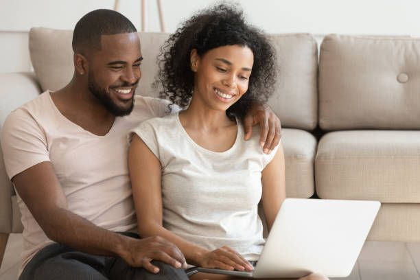 istock Happy african couple using laptop watching movie sit on floor 1170519342