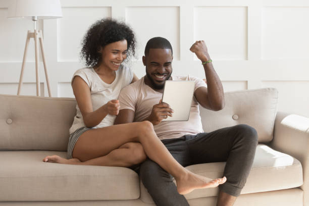 Excited happy african couple looking at digital tablet feel winners