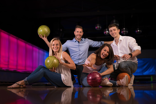 happy young couples four young people friends with bowling balls sitting together smiling at camera