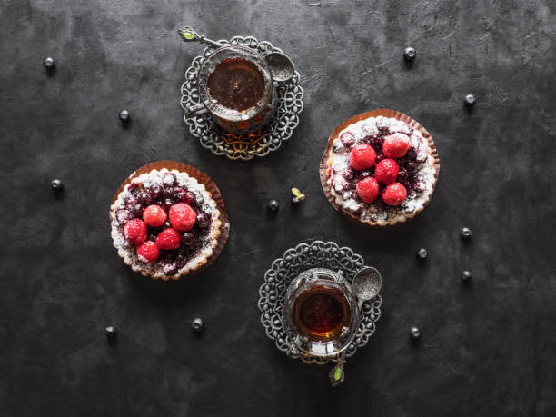 Tea cups, tarts cakes sweets with fresh raspberries and blueberry on black  background
