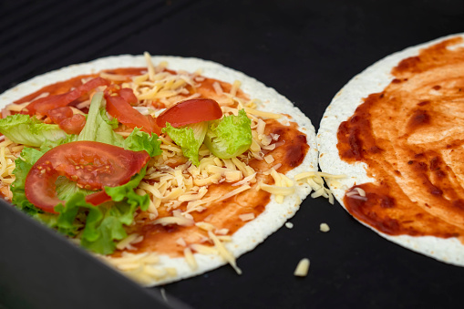 Tortilla pizza with cheese, lettuce, tomatoes close-up. Served very hot, from grill. Concept of national food, healthy fast food
