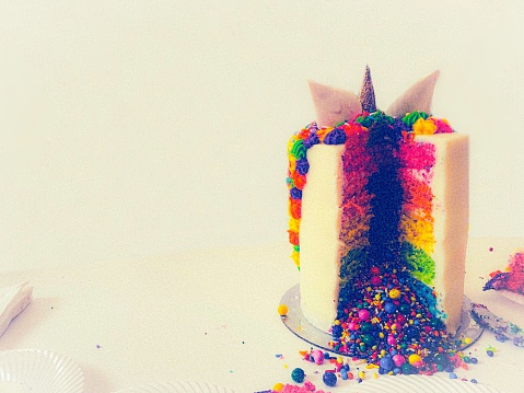 Festive rainbow unicorn cake sliced revealing brightly colored candy and sprinkles.