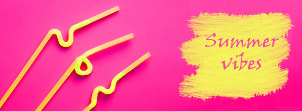 istock Yellow plastic cocktail tubes with a flexible part, due to which they can be twisted into a knot or in a zigzag, on a crimson background. The words SUMMER VIBES is written on yellow drawn stains like a paint. Summer holiday concept 1170528159