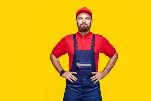 retrato do reparador confiável novo com a barba em geral azul, no t-shirt vermelho e no tampão que estão e que prendem as mãos na cintura com sorriso - coveralls professional occupation manual worker service occupation - fotografias e filmes do acervo