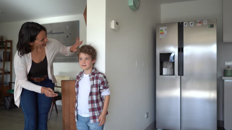 Loving mother measuring son against the wall both celebrating his growth