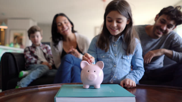 Young parents teaching their kids to save money in a piggy bank on foreground all smiling