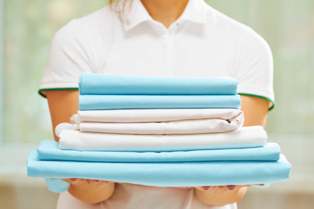 closeup of woman's hand holding a stack of clean folded bed sheets of blue and white colors. blurred background. - service cloth imagens e fotografias de stock