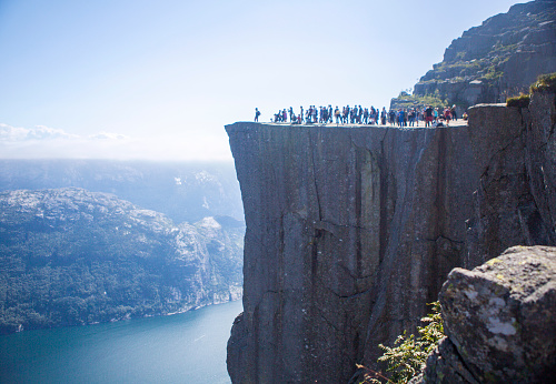 People walking upon Preikestolen, famous nature landmark in Norway. Lysefjorden fjord and mountains in background.