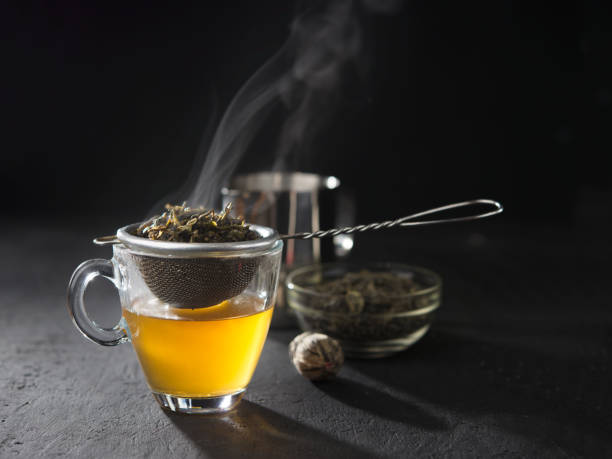 istock Process brewing tea,tea ceremony,Cup of freshly brewed yellow or green herb tea,warm soft light, dark mood.Hot water is poured from the kettle into a cup with tea leaves. 1170554160