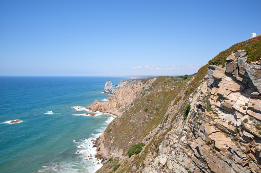 Cape ROCA is the westernmost Cape of Eurasian continent, located on territory of Portugal. Beautiful picture of ocean, hilly terrain, rocks, waves, sky. Famous tourist spot