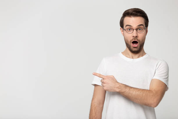 istock Surprised young man wearing glasses pointing finger aside at copyspace 1170564042