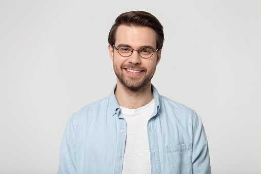 Head shot portrait isolated on grey studio background attractive smiling man wearing glasses blue shirt feels healthy positive posing indoors, representative of millennial gen, optic store ad concept