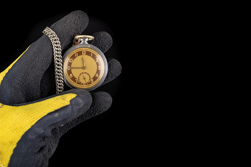 Old analog watch on a work glove. Hand of a production worker in a glove with a watch in his hand. Dark background.