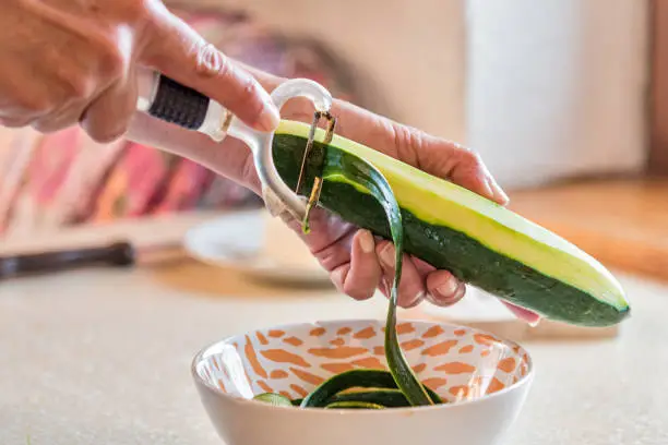 Woman Hands Peeling Cucumber for Making Fresh Mediterranean Salad