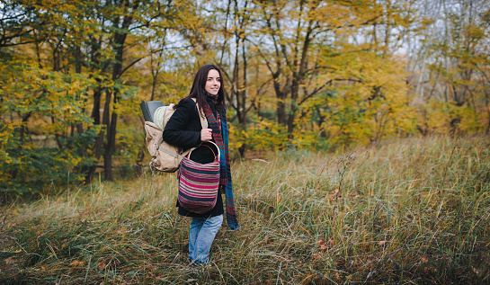 Hiker girl in autumn forest with backpack for camping travel trip. Happy woman hiking outdoors with bag.