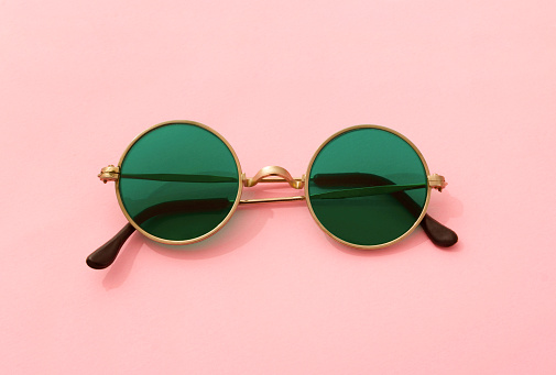 Vintage fashionable round green sunglasses on pink background. Fashion blogger summer beach concept