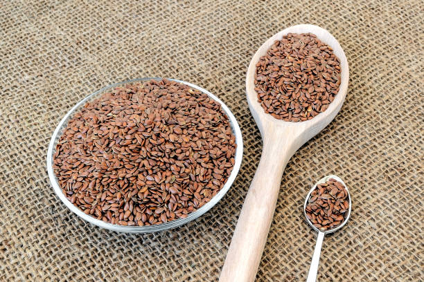 Whole flax seeds in a glass saucer, large wooden spoon and small metall spoon on a sackcloth background. Healthy food for lower cholesterol and preventing heart diseases and cancer. linseed is rich with antioxidants, vitamins, selenium and omega-3. Top view. semillas enteras de lino en un platillo de vidrio, cuchara grande de madera y pequeña cuchara de metal sobre un fondo de saco. alimentos saludables para reducir el colesterol y prevenir enfermedades cardíacas y cáncer. linaza es rica en antioxidantes, v