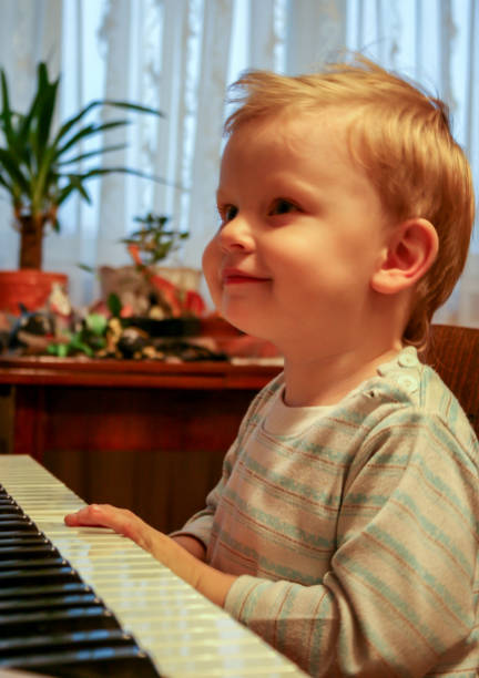 istock Little blonde boy playing piano, side view, blurred and grain effect. 1170582658