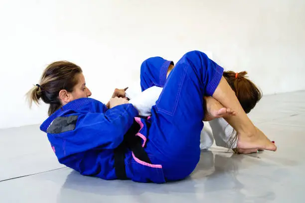 Omoplata submission judo bjj brazilian jiu jitsu training sparring two women female fighters in training wearing kimono gi