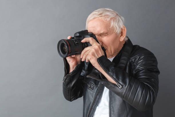 istock Senior man in leather jacket standing isolated on gray taking photos on camera side view 1170598705