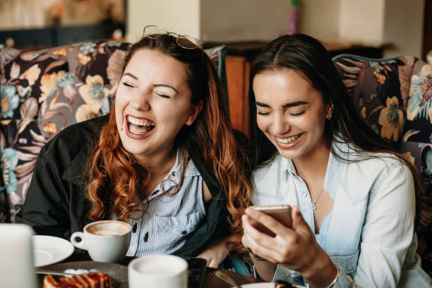 istock Two charming caucasian girlfriend sitting in a cafe and laughing with closed eyes while holding a smartphone. 1170616233