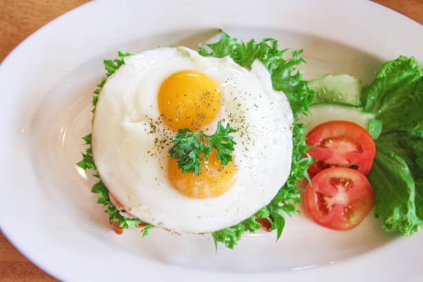 istock Tasty fried eggs on toast bread bacon in sandwich breakfast with fresh organic lettuce , tomatoes and cucumber on white plate top view 1170618160