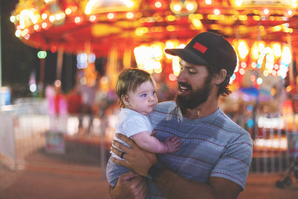 Young Millennial father enjoying time with his infant son at the Empire State Fair in Springfield MO on a hot July summer night At the Empire State Fair in Springfield Missouri a Young Milennial family including father mother and baby boy enjoying their time  on a hot July summer night (Shot with Canon 5DS 50.6mp photos professionally retouched - Lightroom / Photoshop - original size 5792 x 8688 downsampled as needed for clarity and select focus used for dramatic effect) springfield missouri photos stock pictures, royalty-free photos & images