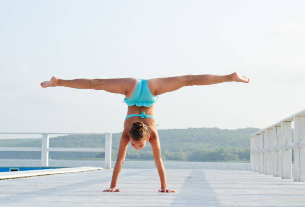 Gymnast little girl child doing acrobatic exercises outdoors on a beach in summer day