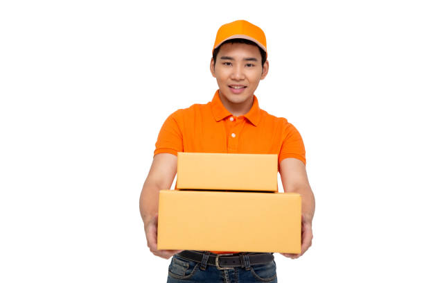 istock Happy young Asian delivery man in orange cap standing with parcel post box isolated over white background 1170633962