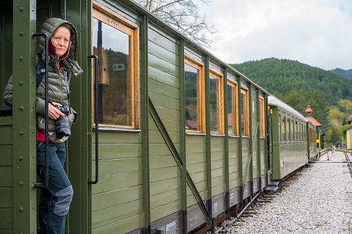 Senior woman standing at the door of Shargan eight railway train in Mokra Gora village, Serbia. It is scenic journeys where train rise upon the hills in the convoluted circles in the shape of number eight.