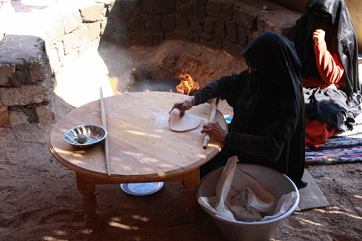 Hurghada, Egypt - November 2012. Bedouine woman in traditional costume cooking a bread on the fire.