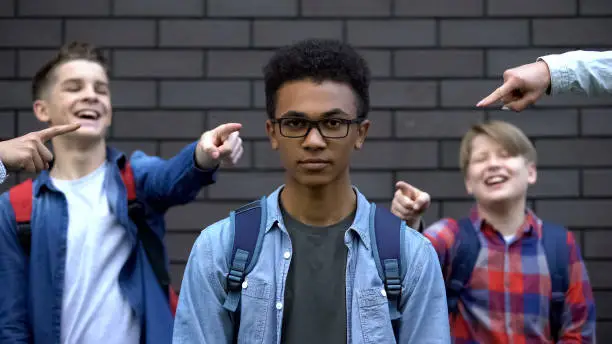 Group of teenagers pointing fingers and laughing at black boy, racial bullying