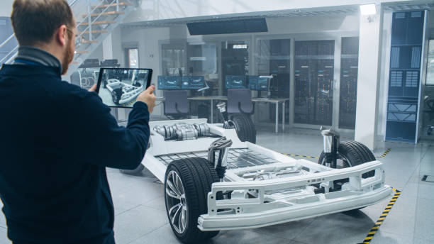 istock Engineer with Glasses and Beard Scans Electric Car Chassis Prototype with Wheels, Batteries and Engine with an Augmented Reality Software on a Tablet Computer in a High Tech Development Laboratory. 1170642903