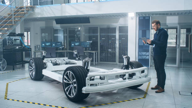 istock Engineer with Glasses and Beard Scans Electric Car Chassis Prototype with Wheels, Batteries and Engine with an Augmented Reality Software on a Tablet Computer in a High Tech Development Laboratory. 1170642911