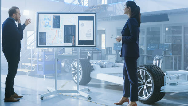 istock Male and Female Design Engineers are Working and Discussing Something on a Interactive Whiteboard Next to an Electric Car Chassis Prototype. In High Tech Laboratory Facility with Vehicle Frame. 1170642914