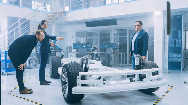 istock Automotive Design Engineers Talking while Working on Electric Car Chassis Prototype. In Innovation Laboratory Facility Concept Vehicle Frame Includes Wheels, Suspension, Engine and Battery. 1170642988
