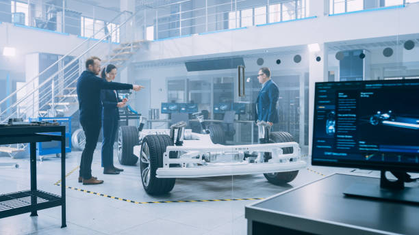 istock Automotive Design Engineers Talking while Working on Electric Car Chassis Prototype. In Innovation Laboratory Facility Concept Vehicle Frame Includes Wheels, Suspension, Engine and Battery. 1170643006