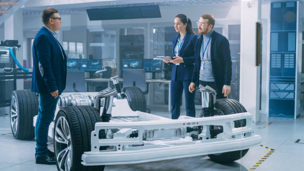 istock Automotive Design Engineers Talking while Working on Electric Car Chassis Prototype. In Innovation Laboratory Facility Concept Vehicle Frame Includes Wheels, Suspension, Engine and Battery. 1170643062