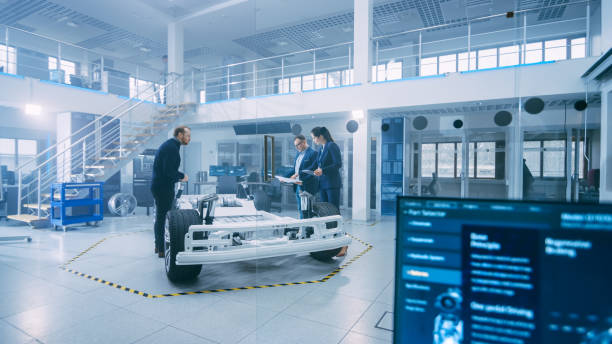 istock Automotive Design Engineers Talking while Working on Electric Car Chassis Prototype. In Innovation Laboratory Facility Concept Vehicle Frame Includes Wheels, Suspension, Engine and Battery. 1170643074