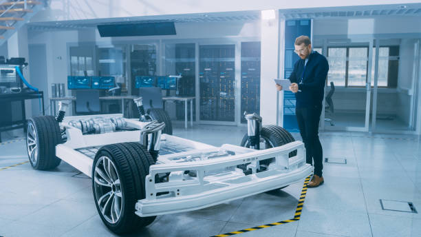 istock Engineer with Glasses and Beard Scans Electric Car Chassis Prototype with Wheels, Batteries and Engine with an Augmented Reality Software on a Tablet Computer in a High Tech Development Laboratory. 1170643089