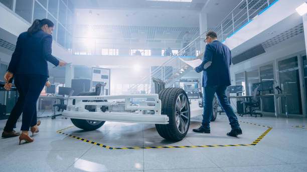 istock Automotive Design Engineers Talking while Working on Electric Car Chassis Prototype. In Innovation Laboratory Facility Concept Vehicle Frame Includes Wheels, Suspension, Engine and Battery. 1170643127