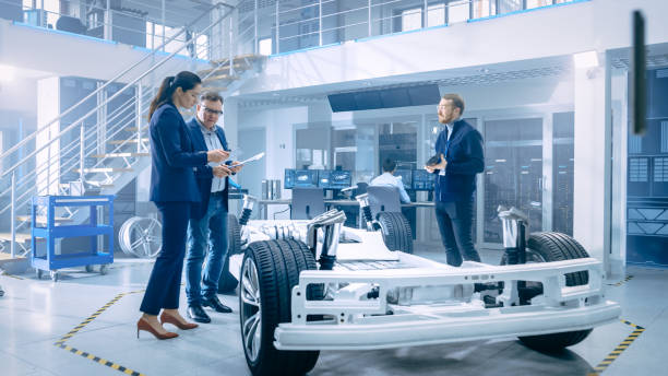 istock Automotive Design Engineers Talking while Working on Electric Car Chassis Prototype. In Innovation Laboratory Facility Concept Vehicle Frame Includes Wheels, Suspension, Engine and Battery. 1170644263